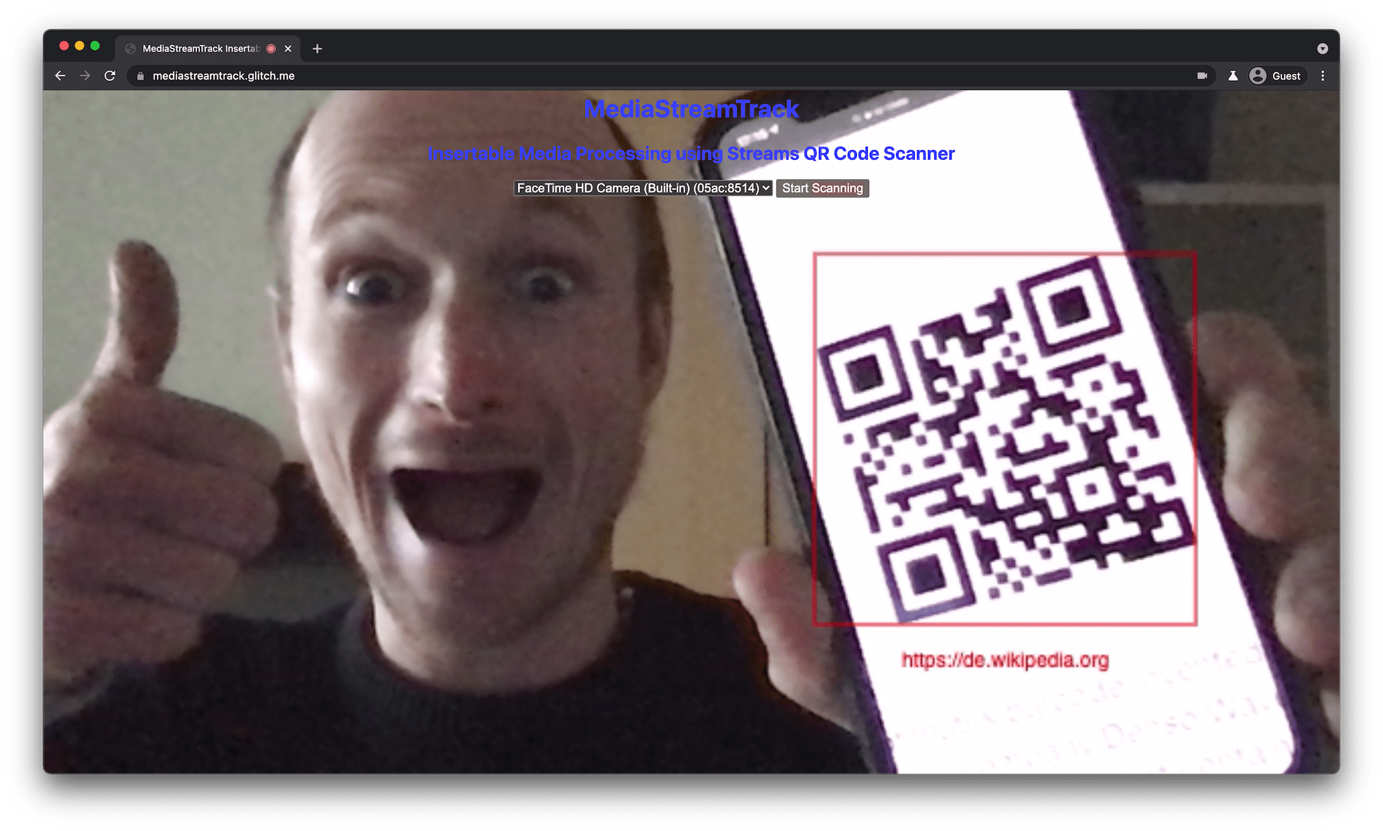 Ein QR-Code-Scanner, der auf einem Desktop-Browser-Tab ausgeführt wird und einen erkannten und markierten QR-Code auf dem Smartphone zeigt, das der Nutzer vor die Kamera des Laptops hält.